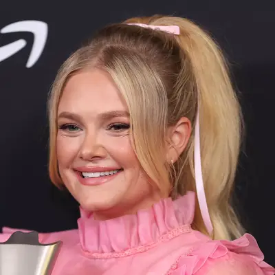 Hailey Whitters wears a high ponytail with a small pink bow, heavy front layers and a high collared, pink frilled dress