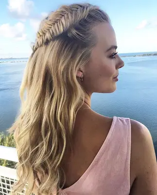 Margot Robbie wearing her blonde hair in a half-up fishtail braid and loose beach waves