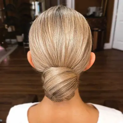 A woman with a sleek and easy blonde low bun hairdo