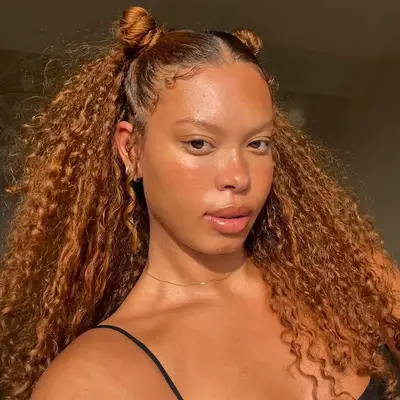 A woman taking a selfie with curly ginger hair in a half-up space bun hairdo