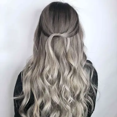 A woman with gray ombrÃ© hair in a tied half-up wavy hairstyle