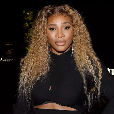 Serena Williams wears a golden beige blonde curly hairstyle and radiant makeup