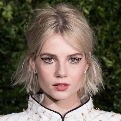 Lucy Boynton wears a bright ash blonde bob in a half-up style and graphic liner