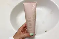 A hand holds a bottle of Vegamour GRO Revitalizing Shampoo over bathroom sink