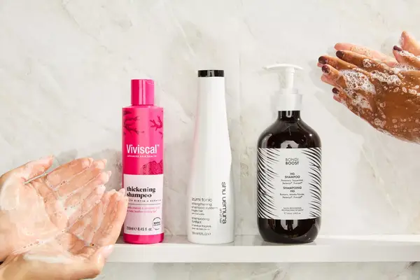 A side-by-side selection of shampoos for thinning hair or hair loss on a shelf surrounded by hands sudsing up