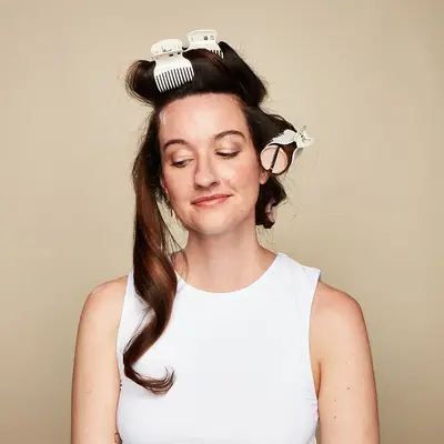 Woman with one tendril of hot rolled hair down; the rest of her hair is in rollers