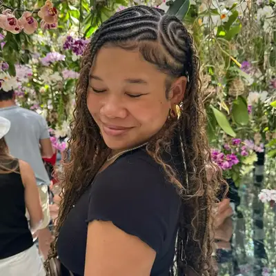 Storm Reid looking down slightly, surrounded by blooming flowers and plants