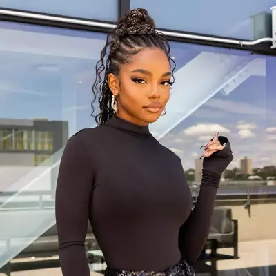 Marsai Martin with styled braided hairstyle in a sleek outfit, posing outdoors with a modern architectural backdrop
