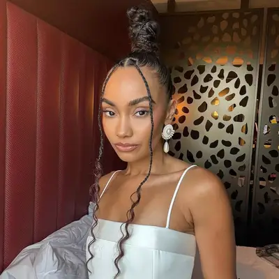 A person with long braided hair wearing a patterned top, looking directly at the camera