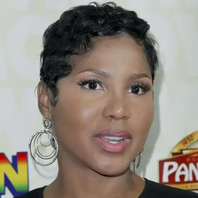 Toni Braxton wears a wavy pixie hairstyle and radiant makeup