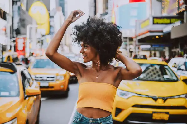 Black woman with natural hair standing in front of taxis in times square