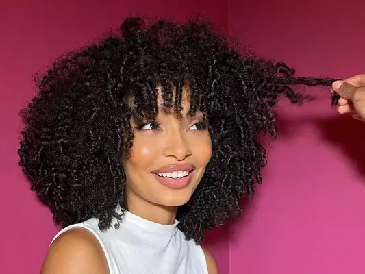 Yara Shahidi wears a voluminous shoulder-length curly hairstyle with bangs