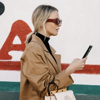 Nadia Fairfax wears a low ponytail and sunglasses while checking her phone