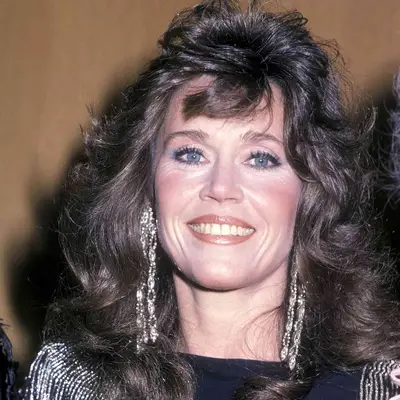 Jane Fonda with dark brown hair in fresh, fluffy blowout, smiling at camera with silver dangling earrings