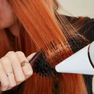 Woman runs brush through her hair as she blow dries