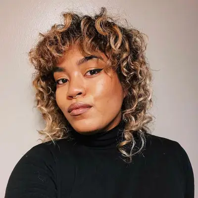 Woman with curly wolf cut with golden blonde highlights and septum piercing