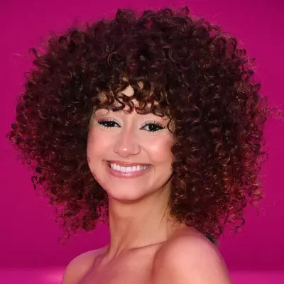 Lena Situations wears a voluminous curly wolf cut hairstyle