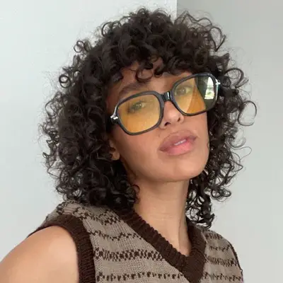 Model wears yellow lensed sunglasses and curly wolf cut hairstyle