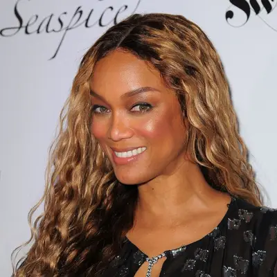 Tyra Banks wears natural curly hair with honey highlights to complement her hazel eyes