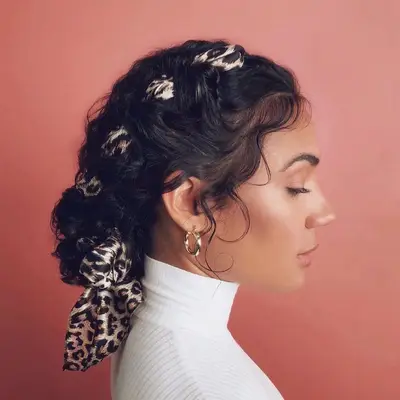 A woman with dark curly hair and a leopard print scarf braided into low bun