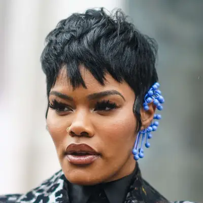Teyana Taylor in a shoppy pixie cut with long sideburns and an ornate blue earring while walking Paris Fashion Week