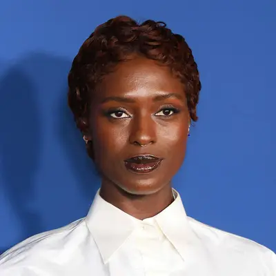 Jodie Turner-Smith attends a screening with a high collar button-up blouse, dark glossed lip, and naturally wavy pixie