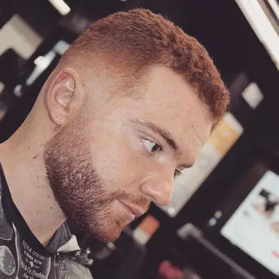 Side view of man with wavy red low fade haircut and defined facial hair