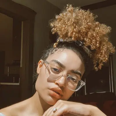 Woman with curly peach-toned hair in high bun