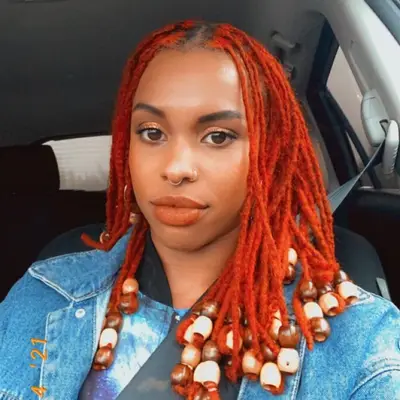Woman with mid-length red-orange locs with beaded ends