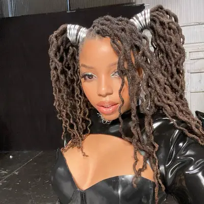 Chloe Bailey wears long, wavy locs in high pigtails with silver thread and face-framing section