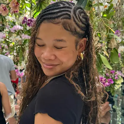 Storm Reid with braided hairstyle indoors among flowers