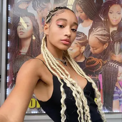 Amandla Stenberg taking a selfie in front of a display showcasing various braided hairstyles
