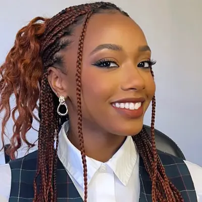 Person with styled braids and earrings, smiling, wearing a white shirt and plaid vest