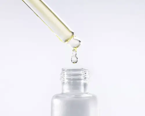 Clear dropper bottle with translucent warm-toned oil dripping