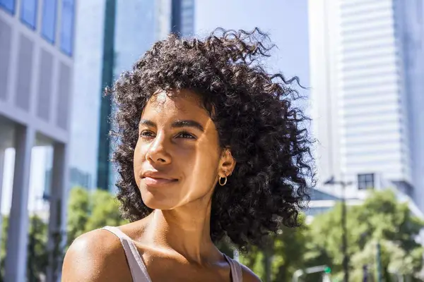 woman with curly hair looking content in front of building
