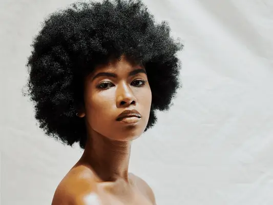 Portrait of a black woman posing with coily afro against a white background