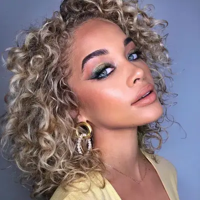Jasmine Sanders wears blonde, curly hair with silver undertones and bold eye makeup