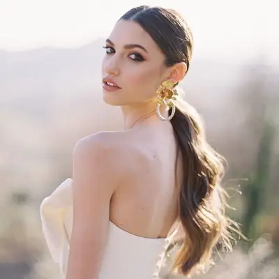 Bride wears a low, loosely curled ponytail and large gold floral earrings