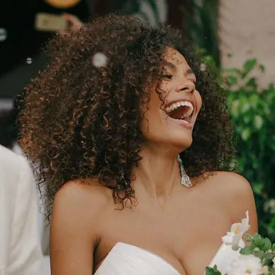 Tina Kunakey wears voluminous natural curls with a sleeveless wedding dress