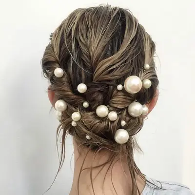 Wet blonde hair in a low updo with pearls placed throughout