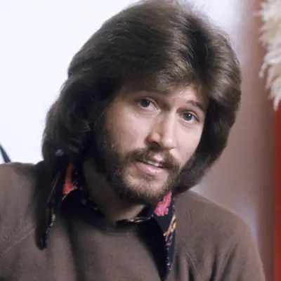 Barry Gibb wears a medium-length hairstyle with feathering and layers