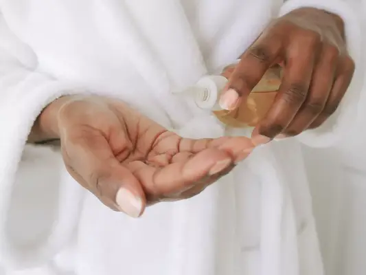 the hands of someone in a robe with one hand holding a bottle of oil and pouring it into the other hand