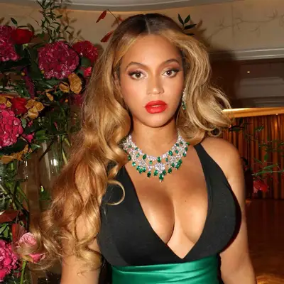 Beyonce with a golden blonde curled blowout with brunette roots, radiant golden skin, and red lipstick