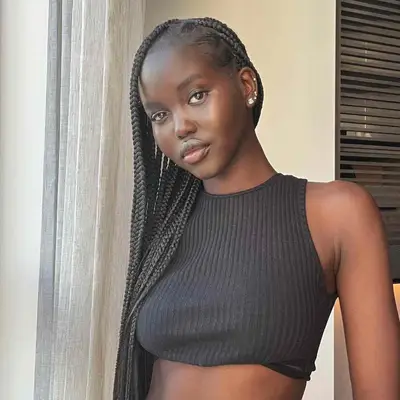 Adut Akech wears long, dark box braids and minimal, cool-toned makeup