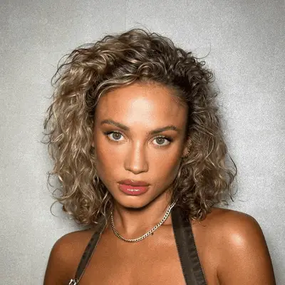 Kelly Rowland smiling in one shoulder green top and side part blonde bob with swoop