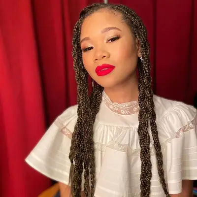 Storm Reid wears braided box braids, red lipstick, and a white ruffled blouse