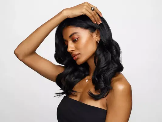Side profile of a model holding her shiny black loosely curled hair behind her ear.