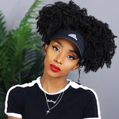 A woman wearing natural curls in an Afro puff style with an Adidas visor