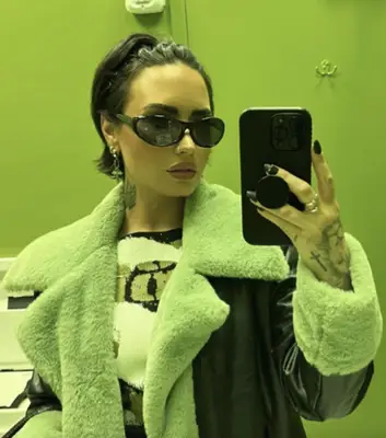 Demi Lovato with zig-zag headband in bixie haircut wearing sunglasses while taking selfie