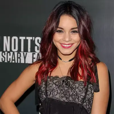 Cardi B wearing a cutout green jacket, a mesh black shirt, and black and white hair